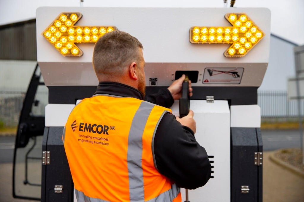 EMCOR employee in an orange high-vis jacket, showing the EMCOR UK logo on the back.