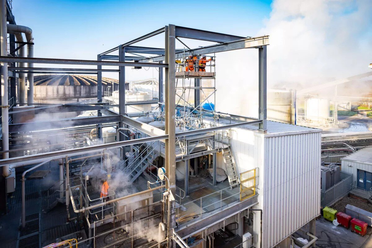 Landscape image of EMCOR UK employees in orange high-vis overalls, working on a structure and standing on scaffolding several stories high.